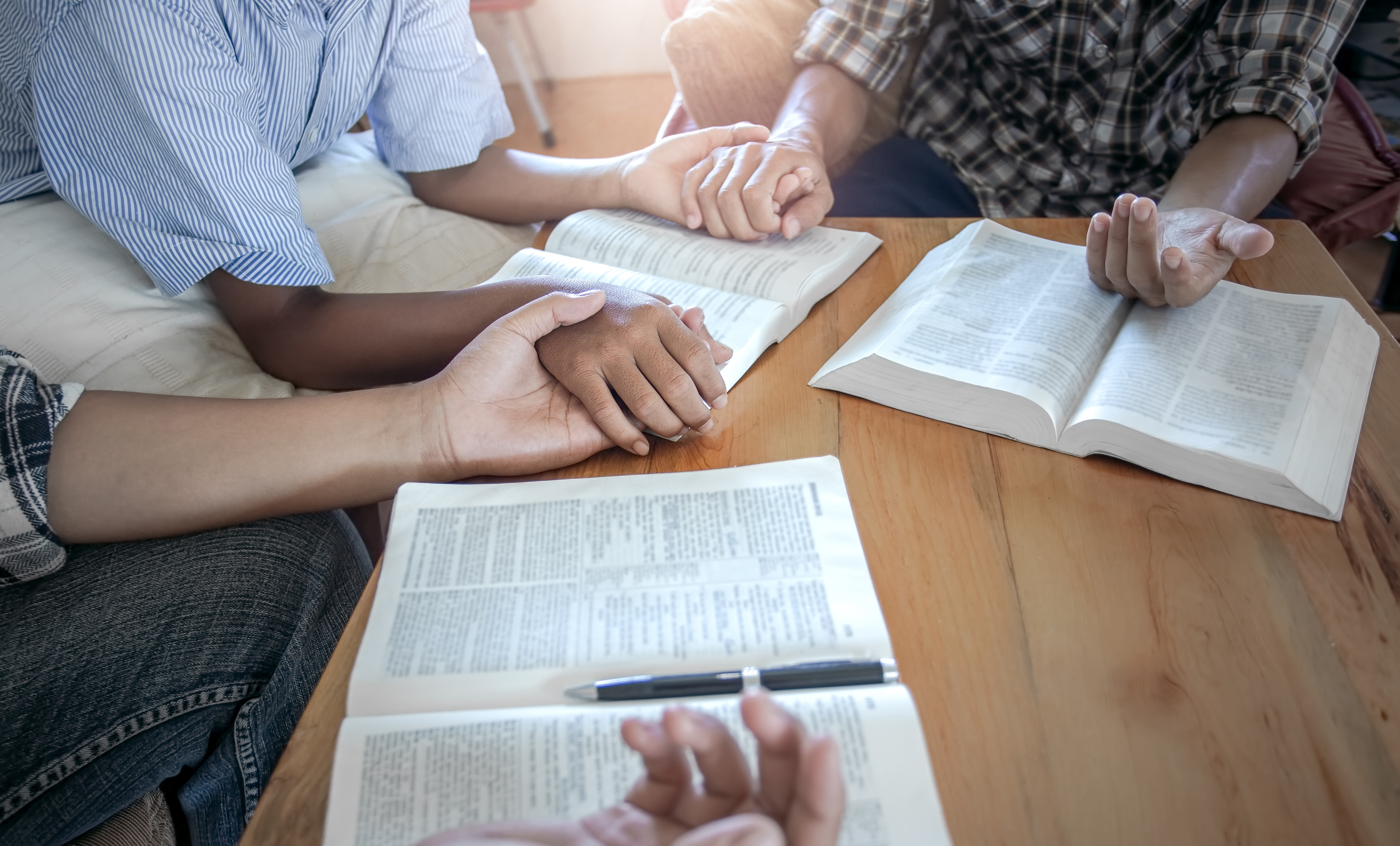 Christian group praying together around wooden table with open b